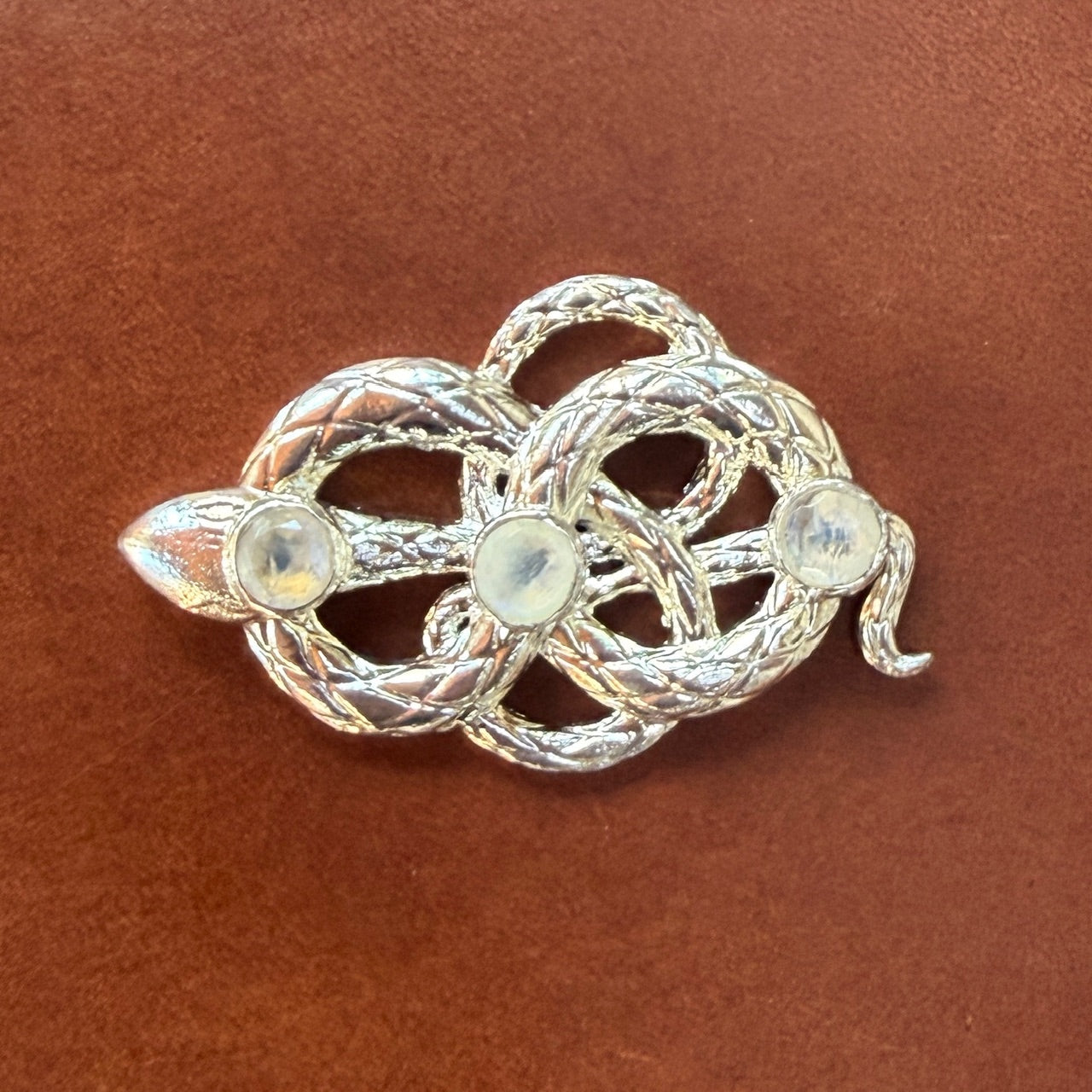 Silver snake buckle with three gemstones on a brown leather background